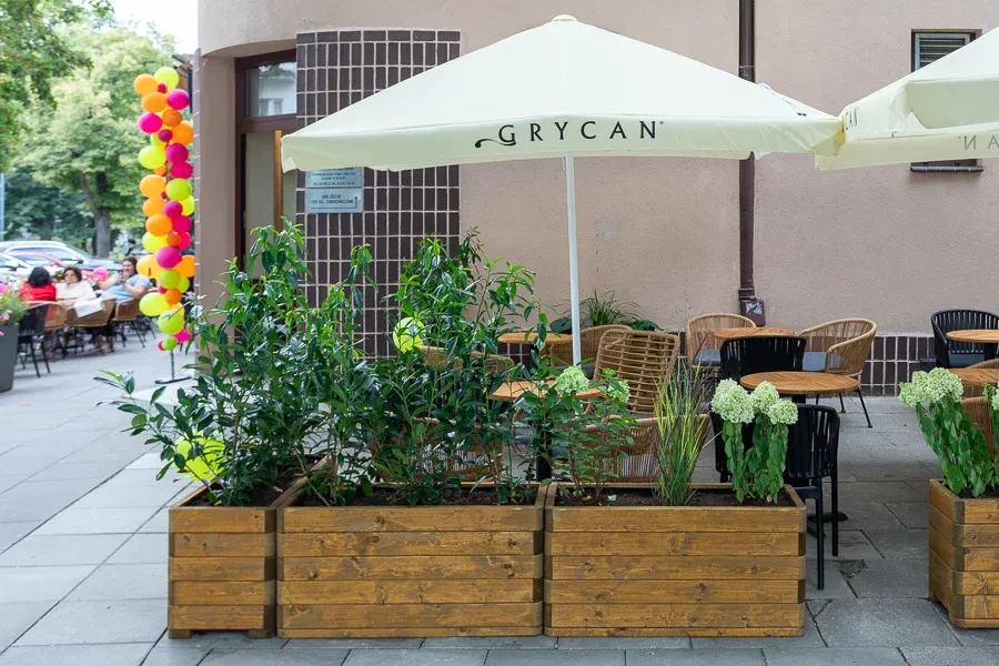 Donica gęsto obsadzona kwiatami i trawami, przy niej stoliki i parasol lokalu