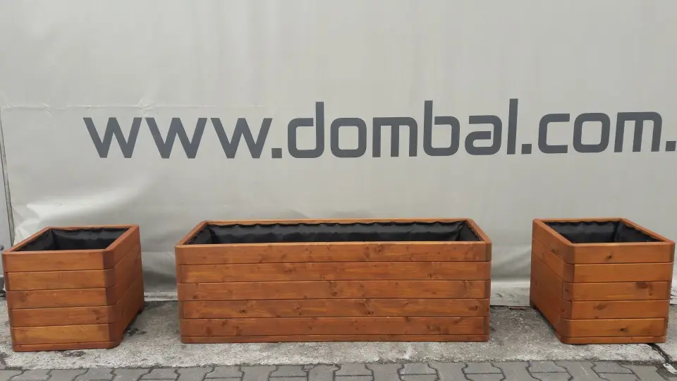 Trzy donice pomalowane na ciepły brąz — dwie kwadratowe i jedna długa prostokątna — ustawione przed banerem firmowym