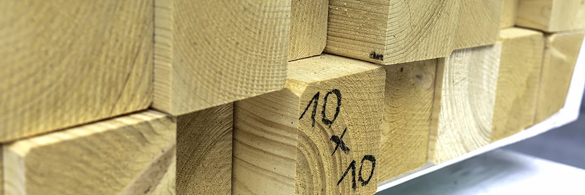 Kantówki KVH złożone w sztaple w magazynie, na czole jednej odręczny napis 10×10
