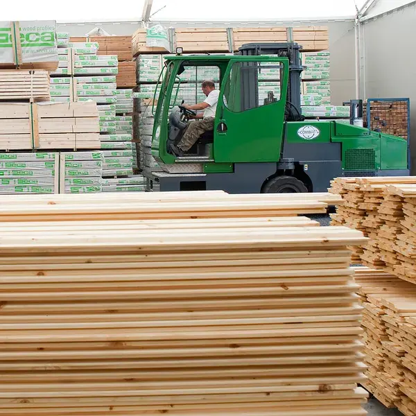 Wózek widłowy Combilift przewozi paczkę desek między stertami drewna konstrukcyjnego w magazynie