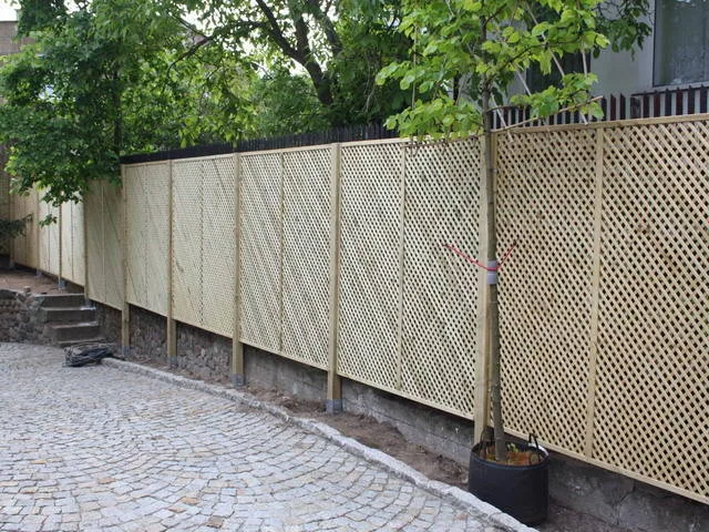 Ogrodzenie z krat o gęstych oczkach, osadzone między słupkami na kamiennym murku wzdłuż podjazdu z kostki brukowej