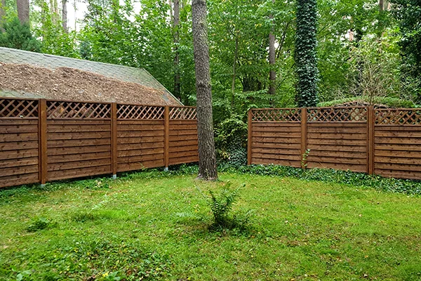 Dwa ciągi ciemnobrązowych paneli z ażurową kratką w górnej części, ustawione pod kątem na leśnej działce