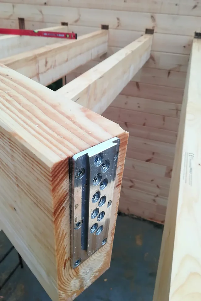 Zbliżenie czoła belki z przykręconą płytką XFIX — dwa rzędy wkrętów z gniazdem torx, w tle konstrukcja stropu