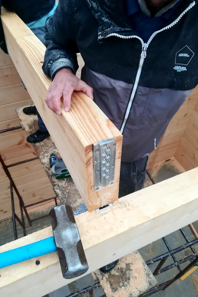 Monter opuszcza belkę z przykręconą aluminiową płytką XFIX na belkę poprzeczną, obok leży młot