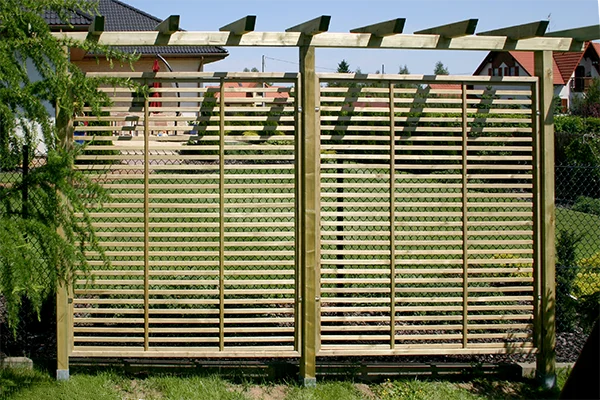 Dwa ażurowe przęsła pod drewnianą pergolą, listwy oplecione zielonym pnączem
