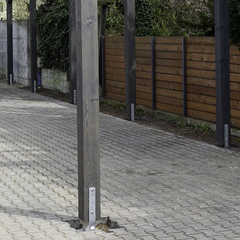 Słup wiaty osadzony na stalowej kotwie zamocowanej w kostce brukowej, drewno nie dotyka podłoża, w tle drewniane ogrodzenie